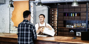 Male owner packing box while talking to customer