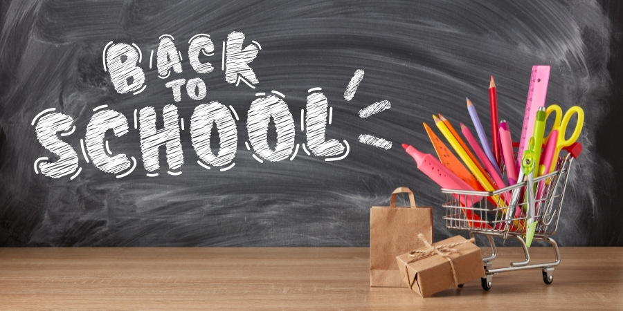 Small shopping cart full of school supplies in front of a chalkboard that says "back to school"