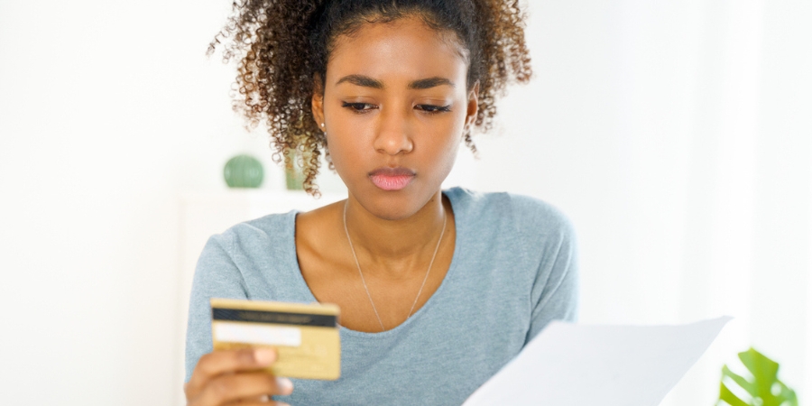 Young woman looking remorsefully at a credit card while also holding the paper bill