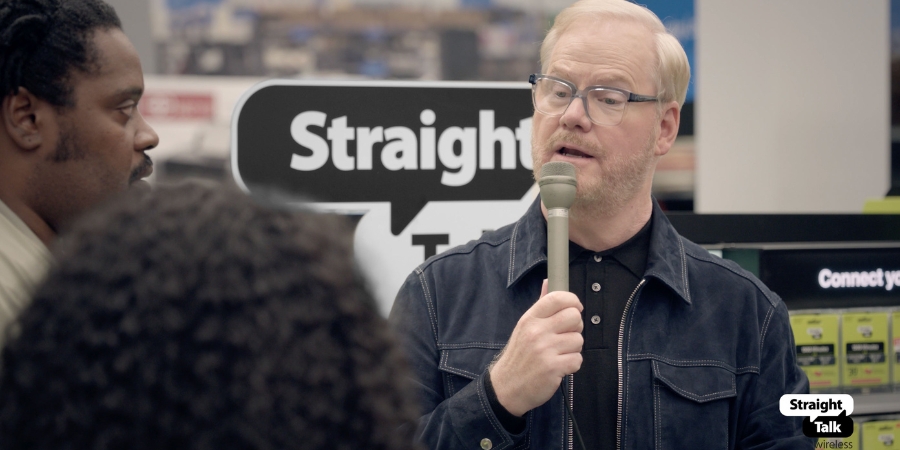 Jim Gaffigan with a microphone in front of a Straight Talk Wireless sign