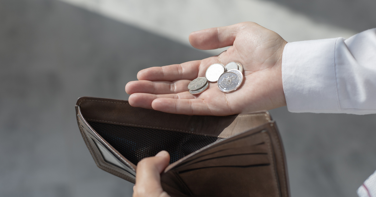 Person holding coins next to an empty wallet
