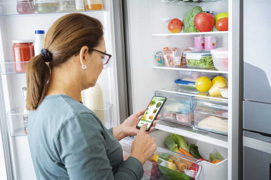 Woman ordering groceries online by the fridge