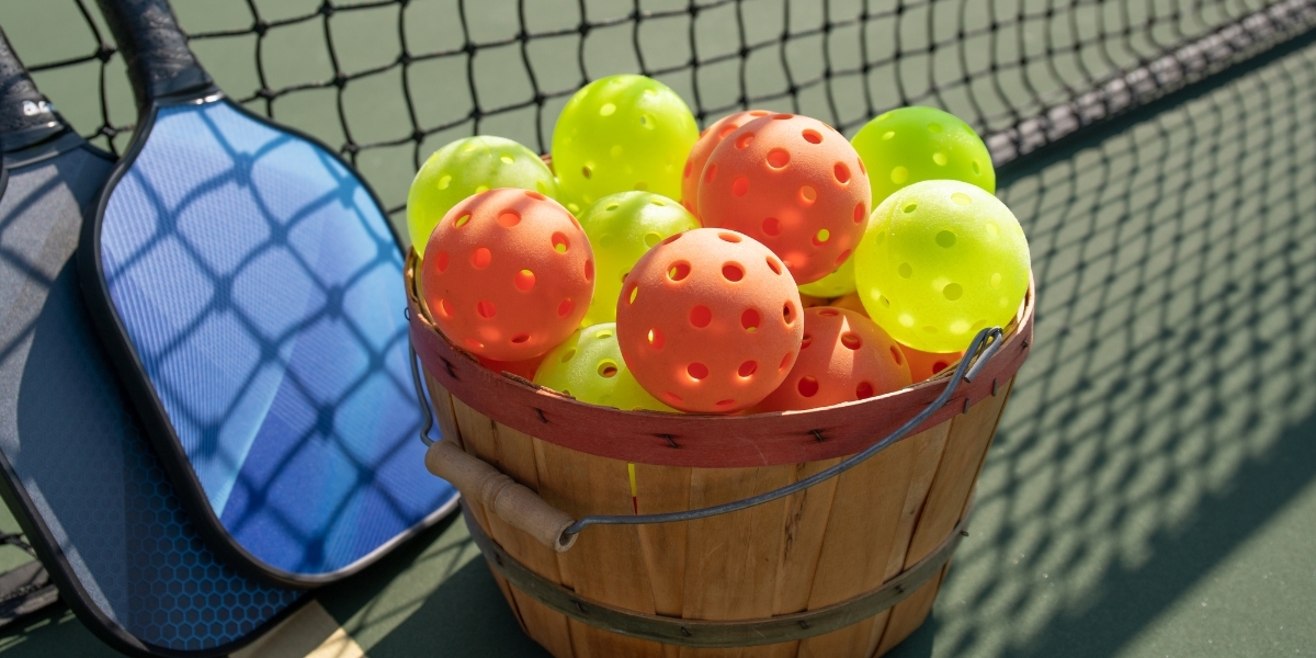 Bucket of pickleball balls next to a racket and net