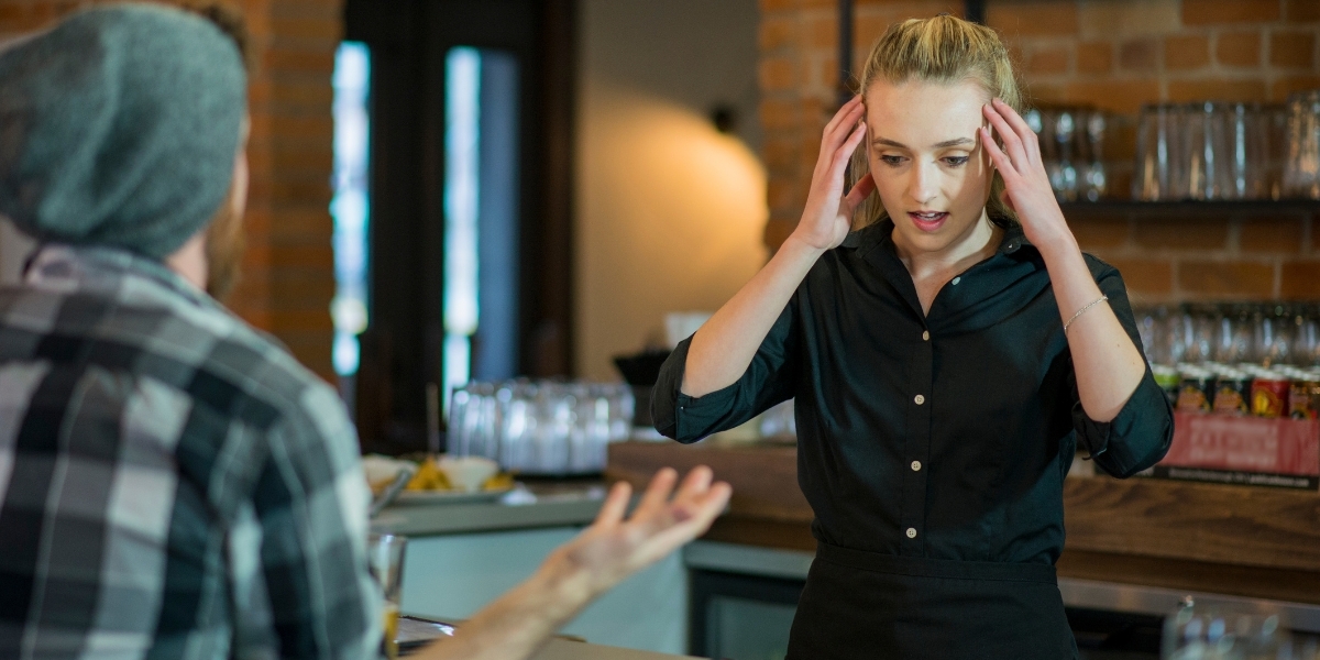 Employee with her hands on her head in front of an upset customer