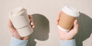 Close-up of someone holding a reusable cup in one hand and a paper cup in the other