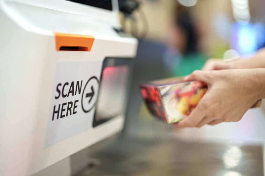 Cropped image of a woman's hands as she scans a grocery item at the self-checkout service in a grocery store.