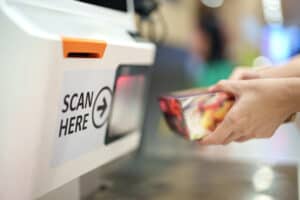 Cropped image of a woman's hands as she scans a grocery item at the self-checkout service in a grocery store.