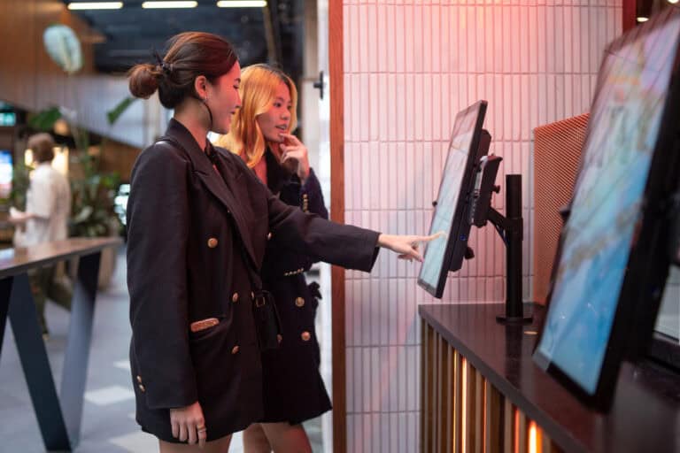 Two Friends Using Touch Screen Self Service Kiosk