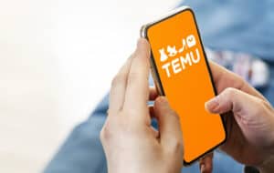 Hands holding a phone with Temu logo displayed on the screen, Temu and Shein. PDD Holdings