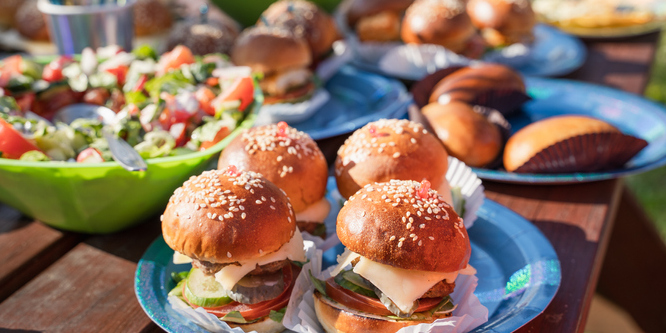 picture of barbecue food outside, with a closeup of four miniature hamburgers, other food in blurred background