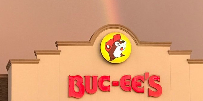 image of Buc-ee's convenience store logo on the front of a store location, beaver mascot in the center, rainbow above store in the sky