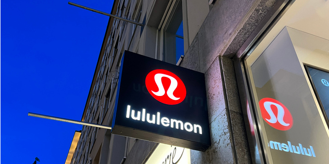 Photo of Lululemon sign, reading lululemon with brand logo above it, taken from below, extending at a right angle from a storefront