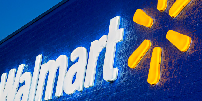 Close up picture of a Walmart sign on a store front, at an angle, lit up at night